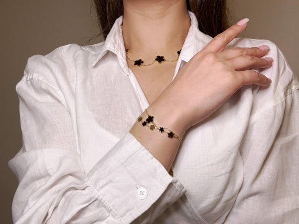 Golden colored stainless steel bracelet with 7 small clovers colored golden and black and one big black clover around wrist.